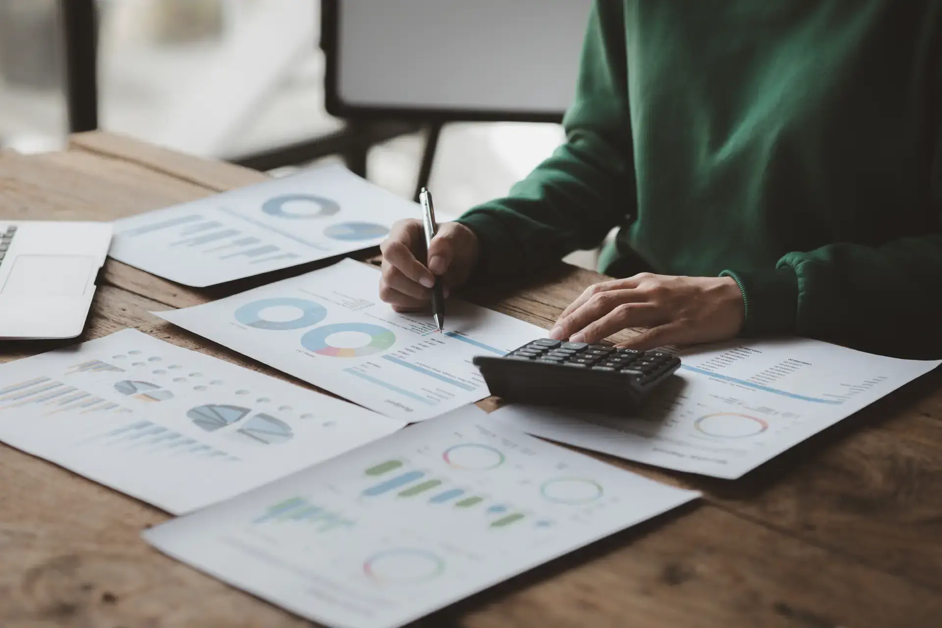 Persona analizando informes financieros con una calculadora y gráficos sobre un escritorio